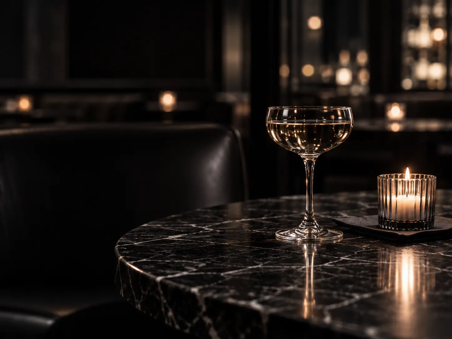 A coupe glass and candle on a dark marble table